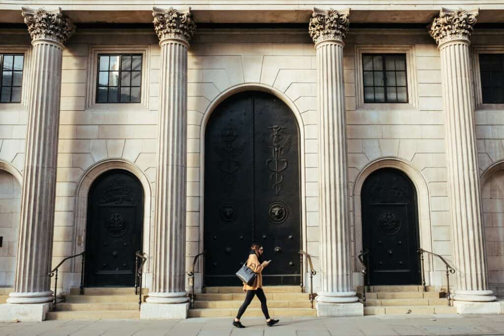 Modern cybersecurity and digital strategy in financial institutions Businesswoman walking past a secure financial institution building, symbolizing modern cybersecurity and digital transformation.